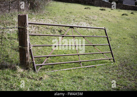 Old metal gate entering a farmer's field broken and hanging from it's hinges. Stock Photo