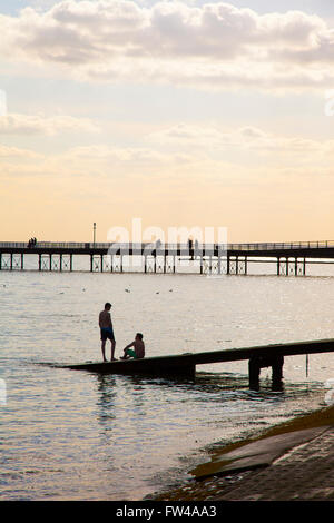 Two boys sitting at the end of a pier with another pier in the background (Southend-on-Sea, Essex, UK) Stock Photo