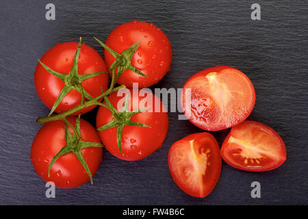 Bunch of cherry tomatoes with slices on dark stone Stock Photo