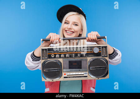 Smiling young woman holding boom box over blue background Stock Photo