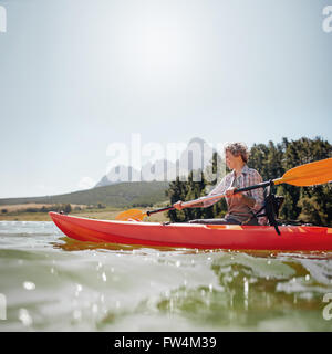 Portrait of a mature woman with kayak in a lake. Senior woman paddling kayak on a summer day. Stock Photo