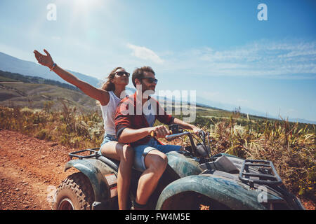 Happy young couple in nature on a quad bike. Young man and woman enjoying a quad bike ride in countryside. Man driving and woman Stock Photo