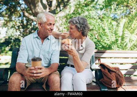 Loving senior couple sitting on a park bench having coffee and muffins. Tourist relaxing outdoors on a park bench.