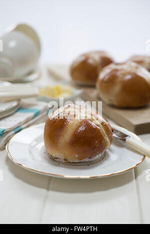 Homemade hot cross buns on a cream painted table set with fine china plates and cups. Stock Photo