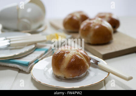 Homemade hot cross buns on a cream painted table set with fine china plates and cups. Stock Photo