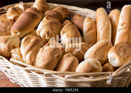 Wicker basket filled with assorted freshly baked crusty bread rolls in different shapes on display at a bakery Stock Photo