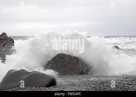 A slow shutter seed captures a wave crashing onto rocks during low tide at a West Coast beach, South Island, New Zelaand Stock Photo