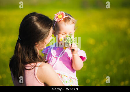 Little girl smelling field flowers. Family enjoying nature on spring or summer warm day outside Stock Photo