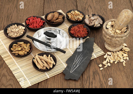 Acupuncture needles, moxa sticks, traditional chinese herbs for herbal medicine and mortar with pestle over bamboo and old oak. Stock Photo