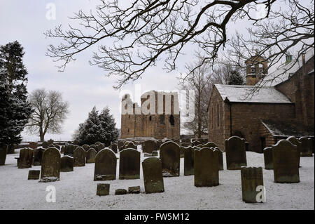 Bowes Church, the ruins of the castle, and graves under snow, on the Yorkshire Moors (now in Co. Durham), by the A66. Here are buried the original of Smike, companion to Nicholas Nickleby in the novel by Charles Dickens, English author, and William Shaw, headmaster, along with 8 pupils from William Shaw's Academy, one of several schools in the area offering tuition 'without holidays' to unwanted children, often from London. Dickens made a special visit through thick snow in February 1838, and denounced the cruelty and appalling conditions in his novel, carefully naming the headmaster 'Wackford Stock Photo