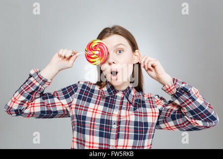 Surprised cute teenage girl in checkered shirt covered her eye with lollipop Stock Photo