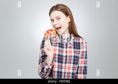 Happy attractive teenage girl in plaid shirt standing and eating lollipop Stock Photo