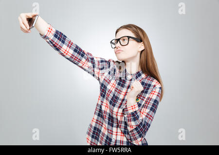 Playful charming teenage girl in checkered shirt and glasses taking selfie with cell phone Stock Photo