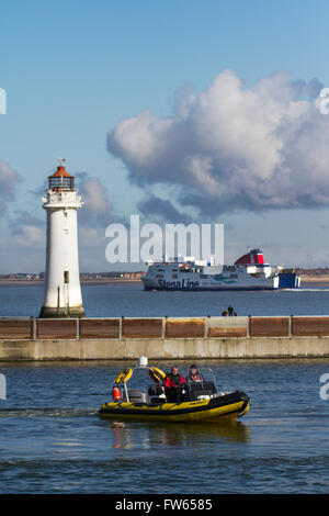 RNLI training on the boating lake, with shiping leaving the River Mersey heading for the Irish sea passing Fort Perch Lighthouse, New Brighton, Wallasey, Merseyside, UK Stock Photo