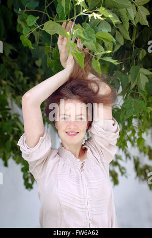 Young woman in the park. Inspiration. Breathing, relaxation, atmosphere. Summer mood. Portrait of a girl hair in leaves smiling Stock Photo