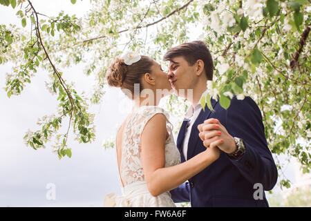 elegant stylish groom with his happy gorgeous brunette bride on the background of apple trees blossom in the park