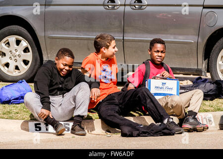 three laughing preteen boys sit on a neighborhood curb together in Oklahoma City, Oklahoma, USA. African American, Hispanic. Stock Photo