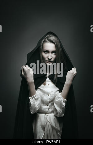 Dark portrait of a beautiful vampire with black hood . Halloween and horror concept Stock Photo