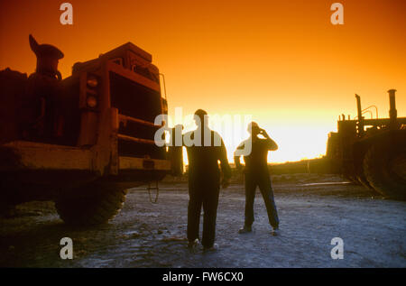 Construction Workers Talking on a Cellphone Beside an Earth Mover at Sunset Stock Photo