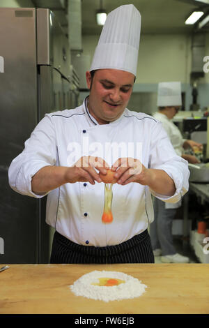 A chef cracking a egg to making fresh pasta in kitchen with apprentices in the background,Gubbio,Umbria,Italy Stock Photo