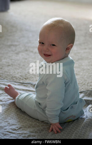 A happy 8th month old baby boy smiling, and sitting on floor wearing a light blue romper. Stock Photo