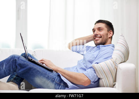 smiling man lying on couch with laptop at home Stock Photo