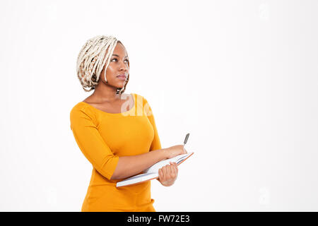 Thoughtful pretty young african american woman writing in notebook and thinking over white background Stock Photo