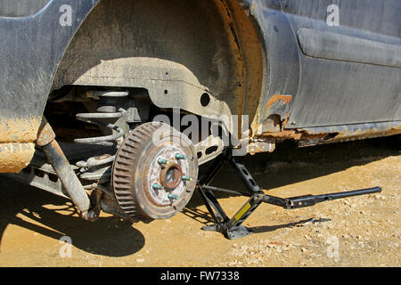 An old rusty automobile is lifted up on a jack with the wheel removed to change the tire. Stock Photo