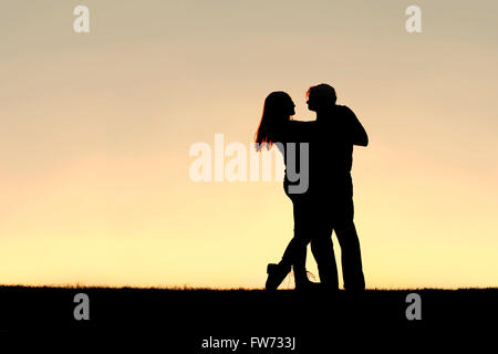 A silhouette of a happy young married couple slow dancing outside at sunset, with copy-space in sky. Stock Photo