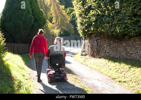 Rear view of an elderly man using a mobility scooter with his carer walking beside him Stock Photo