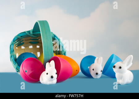 Easter basket filled with plastic eggs rolls over and little white bunnies hatch from cracked eggs Stock Photo