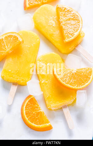 Homemade, natural orange ,refreshing summer popsicle. From above flat lay on white marble with fresh orange slices. Stock Photo