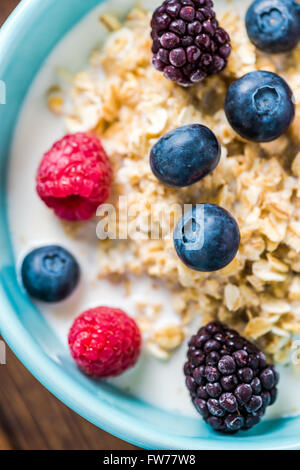 Bowl with oat porridge and berry fruits, view from overhead on wooden rustic table. Stock Photo