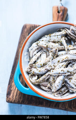 Anchovy with herbs in traditional tapas ceramic bowl, from overhead on wooden board Stock Photo