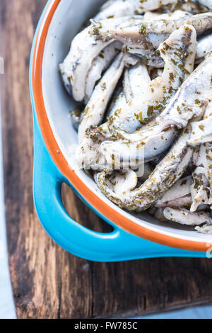 Anchovy with herbs in traditional tapas ceramic bowl, from overhead on wooden board Stock Photo