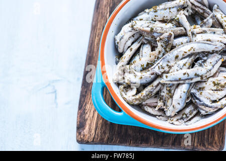 Anchovy with herbs in traditional tapas ceramic bowl, from overhead on wooden board Stock Photo