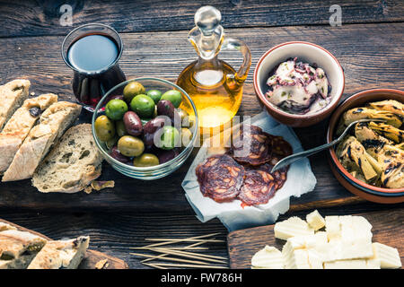 Tapas served in restaurant or bar on wooden table, with red wine meat and bread. Stock Photo