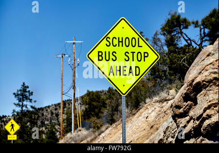 School Bus Stop Ahead sign with pedestrian crossing sign in background and mountain terrain Stock Photo