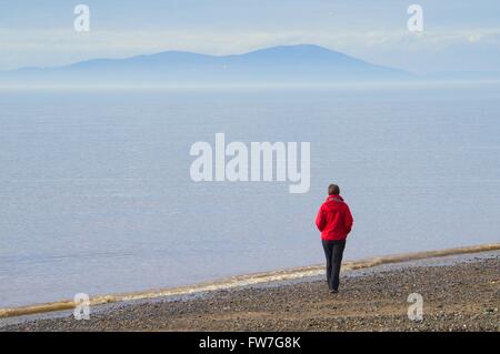 Lonely Woman walking on beach with Criffel in distance. Allonby, Cumbria, England, United Kingdom, Europe. Stock Photo