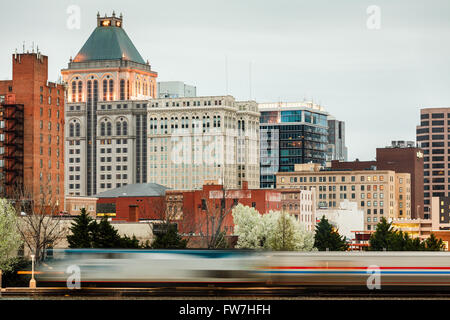 Amtrak train departs beneath city skyline, Greensboro, North Carolina, USA. Stock Photo