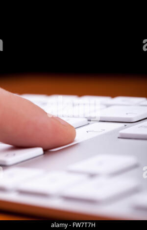 Finger pressing an enter button on alluminium keyboard with black copy space on top of it Stock Photo
