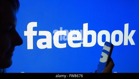 A woman's silhouette with a smartphone in front of a facebook logo, 23 March 2016. Stock Photo