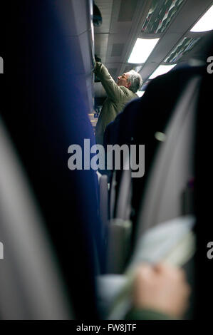 A man stows his bag in an overhead locker or baggage rack on a train in the UK. As the journey begins and the train departs bags are placed out of the way to make room for the passengers on the train. Stock Photo