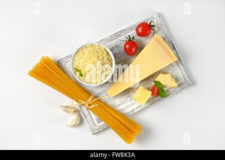 fresh parmesan cheese, vegetable garnish and bundle of raw spaghetti on wooden cutting board Stock Photo