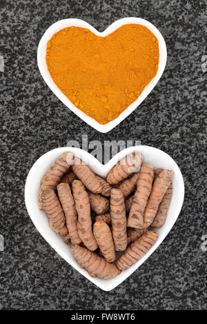Turmeric spice fresh and dried powder in heart shaped porcelain bowls over marble background. Stock Photo