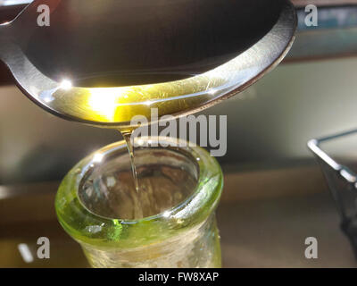 Pouring olive oil from the spoon to the glass oil cruet Stock Photo