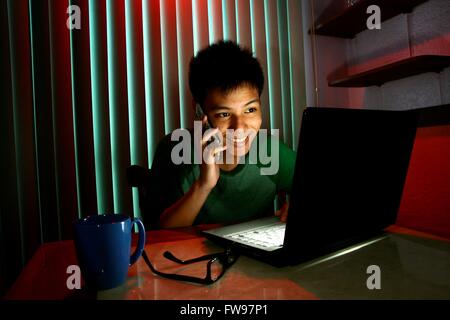 Teen using a cellphone or smartphone in front of a laptop computer Stock Photo