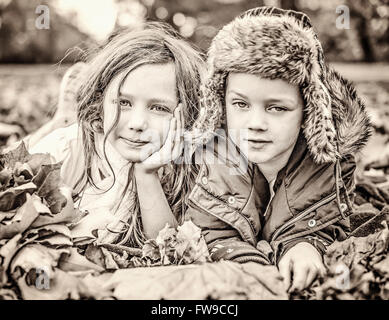 two children lying on autumn grass in park Stock Photo