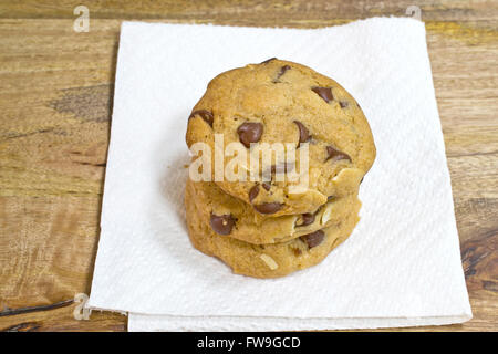 Three chocolate chip and shredded almonds cookies  piled up over paper towel, on aged wooden table Stock Photo