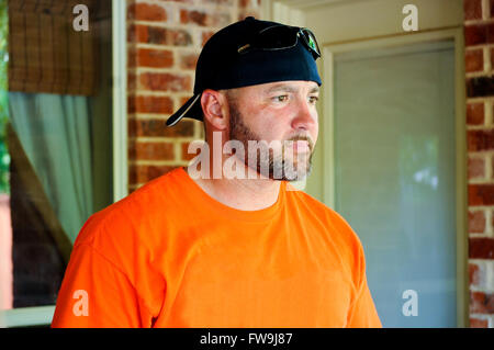 Serious man in beard and backwards hat in orange shirt. Stock Photo